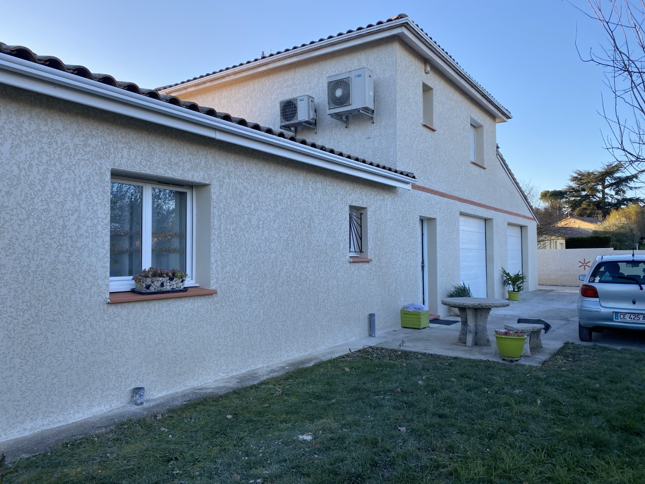 Maison avec enduit texturé blanc avec jardin engazonné, petites fenêtres et voiture, après un ravalement de façade
