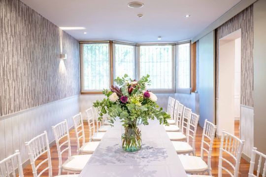 Una mesa larga con un jarrón de flores encima en una habitación con sillas.