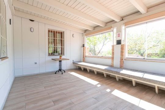 Una habitación con una mesa y bancos y muchas ventanas.