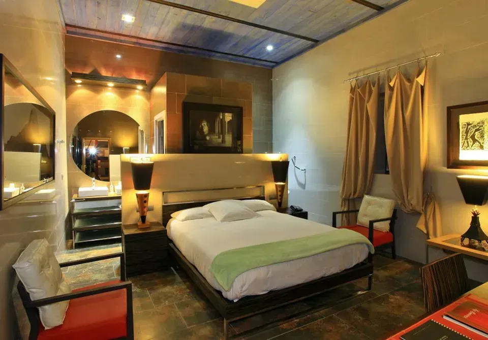 Dormitorio con cama, dos sillas y baño parcialmente visible; iluminación cálida y diseño moderno.