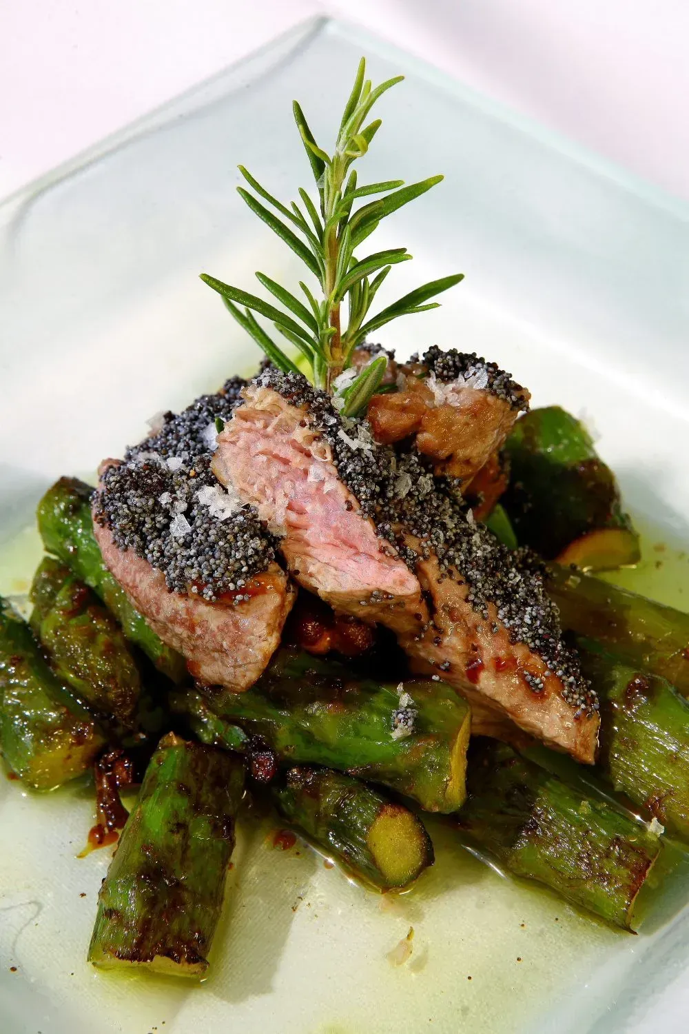 Filete rebanado con costra negra y romero, servido sobre verduras verdes salteadas.
