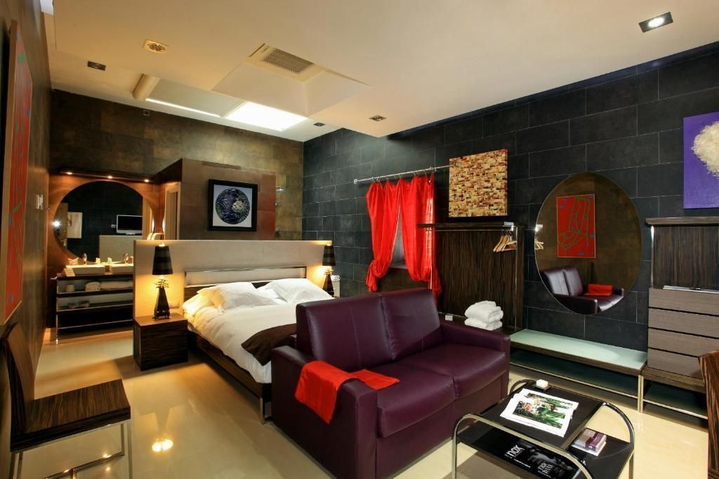 Habitación de hotel con una cama, un sofá blanco, una mesa pequeña sobre una alfombra, techo de madera y paredes de color rojo oscuro.