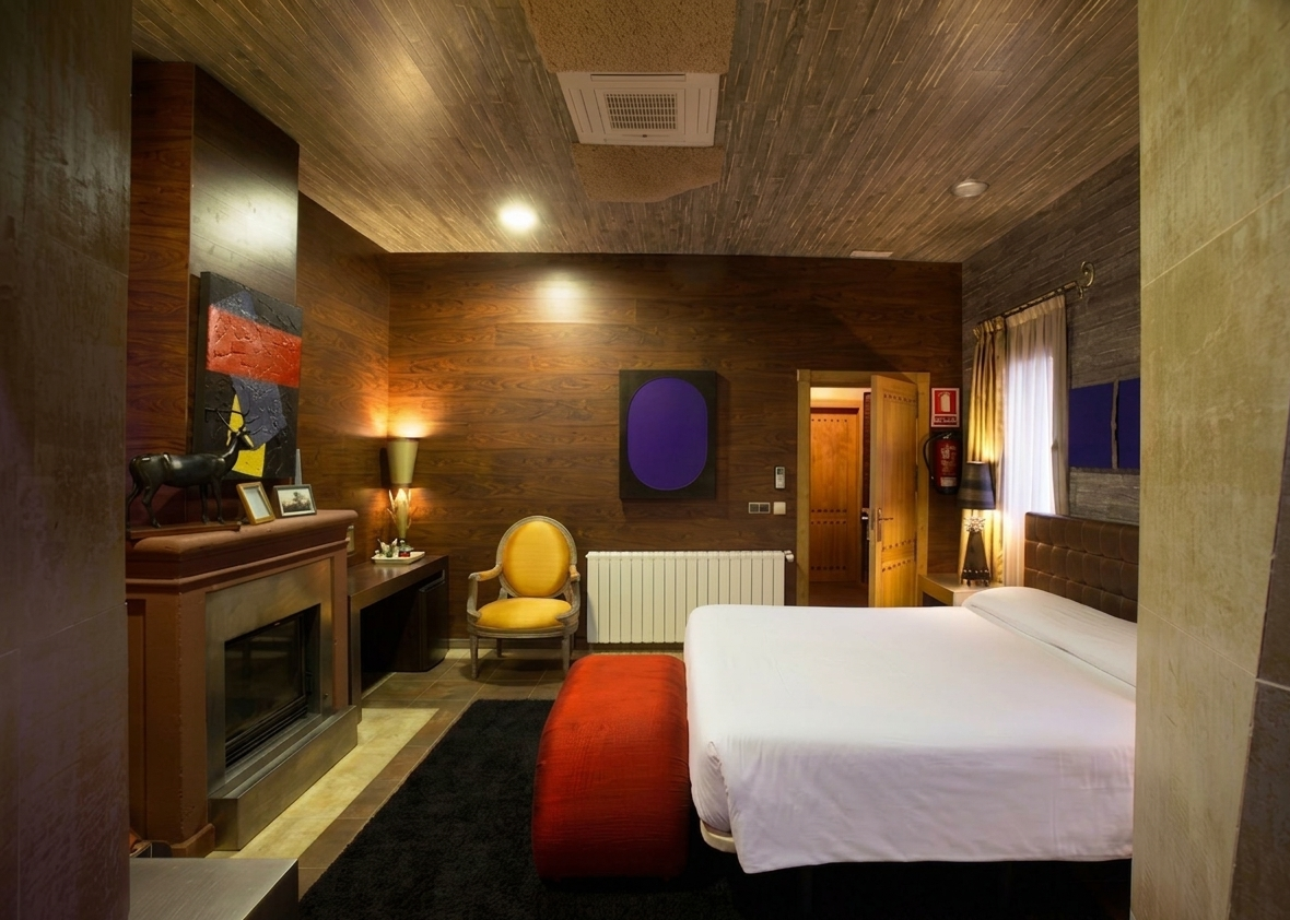 Habitación de hotel con cama, sillas y obras de arte. Cortinas naranjas y doradas, techo azul.