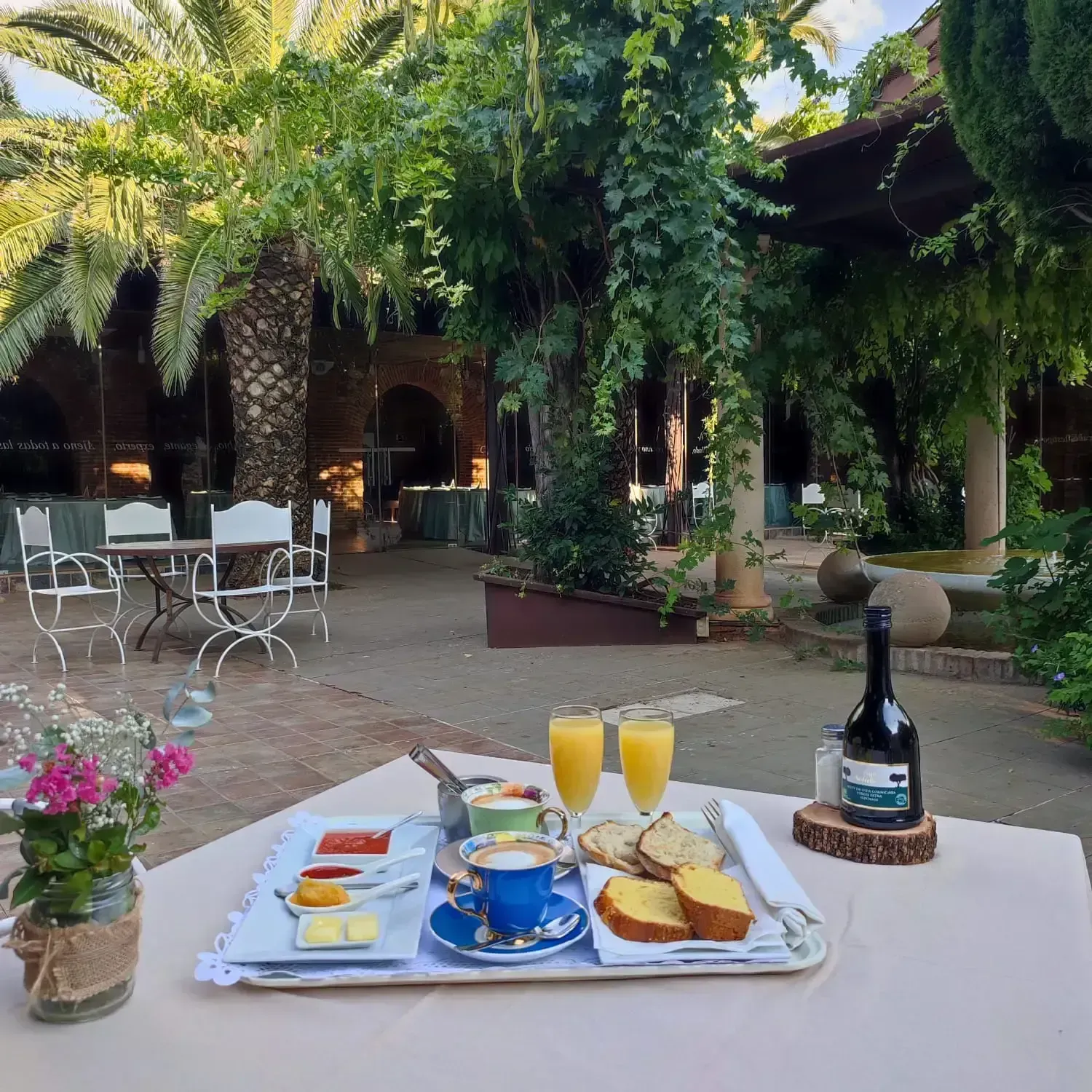 Bandeja de desayuno con café, bollería y zumo al aire libre en un entorno de patio.