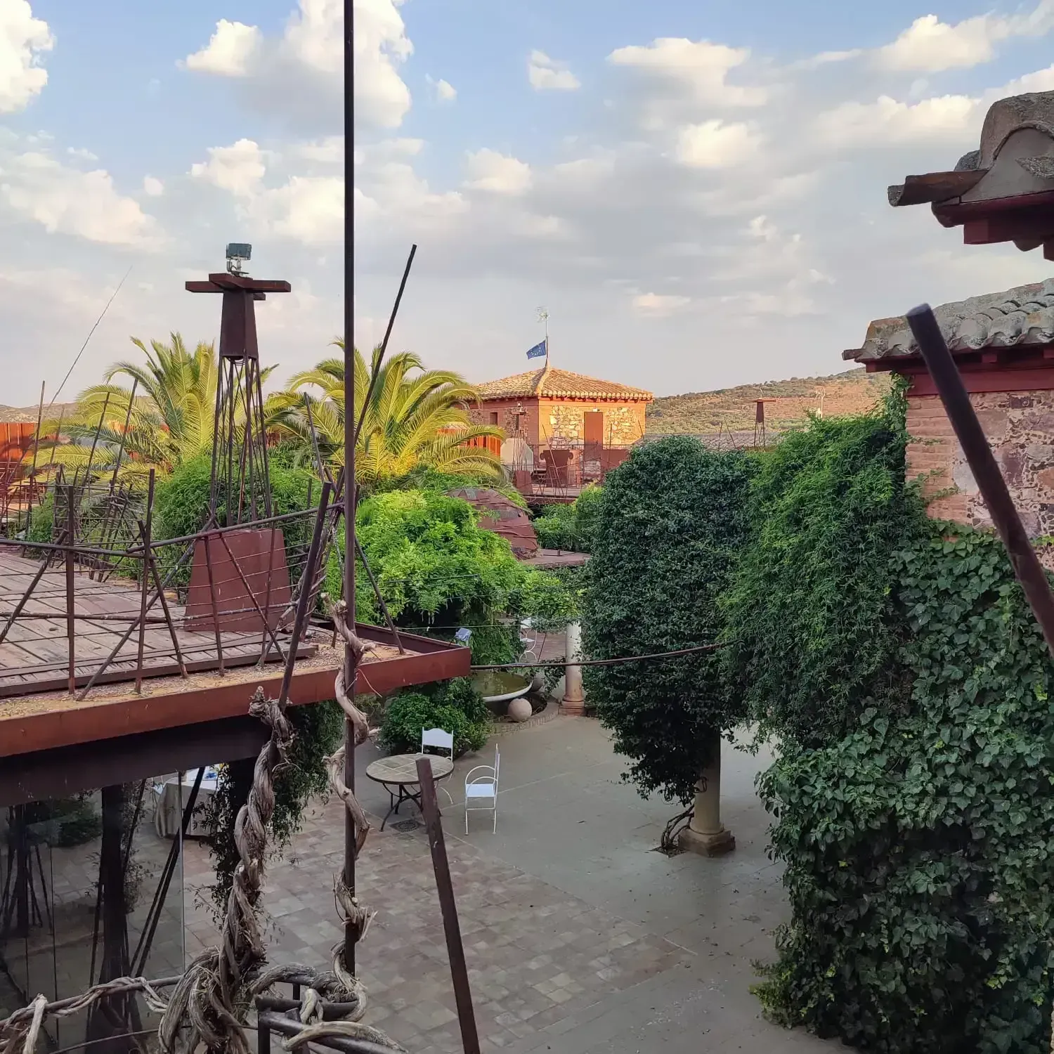 Patio con edificios de ladrillo, árboles y un molino de viento contra un cielo parcialmente nublado.