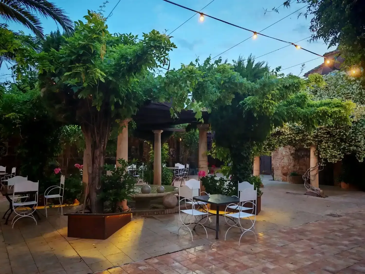 Comedor con mesa redonda preparada para invitados, sillas blancas, arte de pared colorido y entrada arqueada.