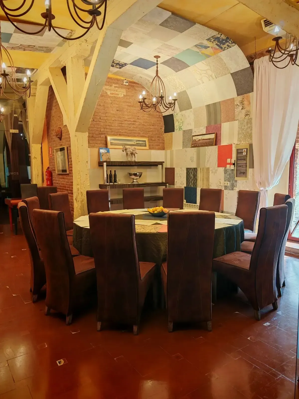 Comedor con mesa redonda preparada para invitados, sillas blancas, arte de pared colorido y entrada arqueada.