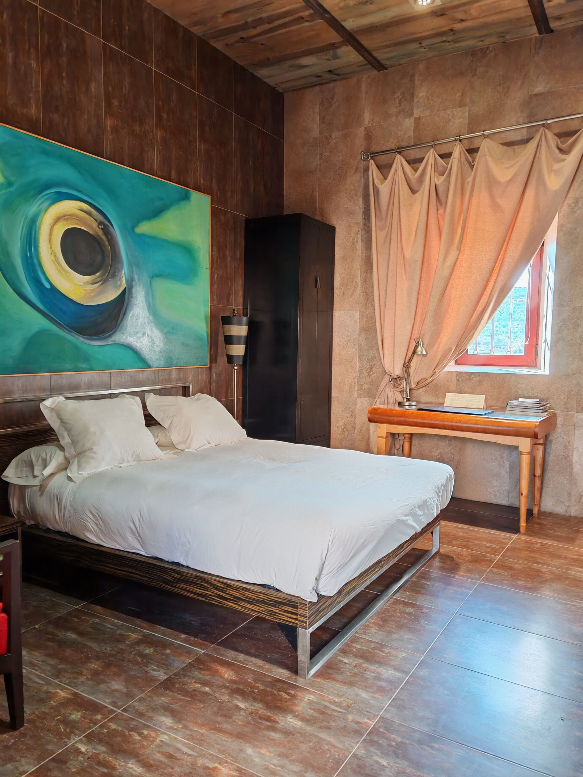 Dormitorio con dos camas individuales, paredes de madera en varios colores, lámpara de araña, puerta de acceso al baño.