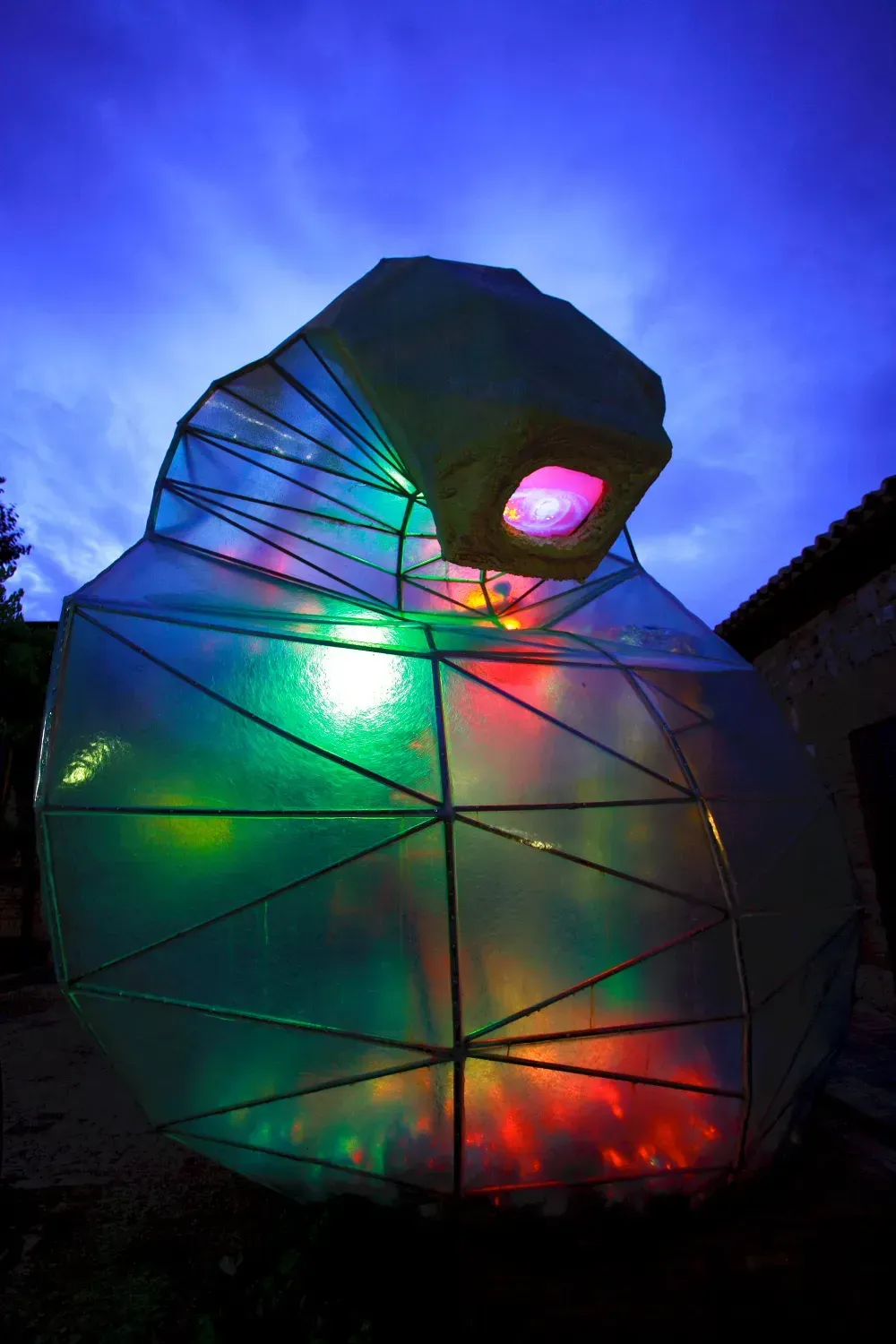 Estructura abstracta e iluminada con luces de colores contra un cielo azul oscuro.