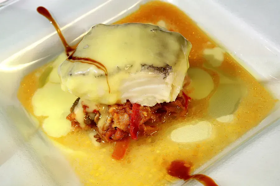 Filete de pescado con salsa sobre una cama de verduras, servido en un plato cuadrado blanco.