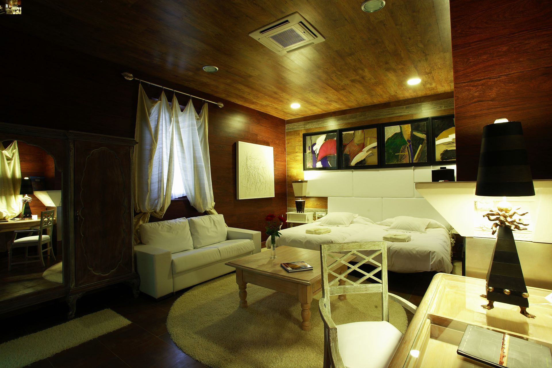 Habitación de hotel con cama, sillas y obras de arte. Cortinas naranjas y doradas, techo azul.