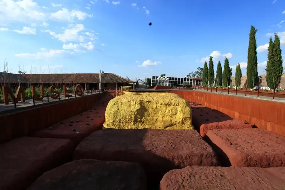 Una instalación de arte al aire libre: una fuente de agua rectangular con grandes bloques de color marrón rojizo; una forma rectangular de color dorado en el centro.