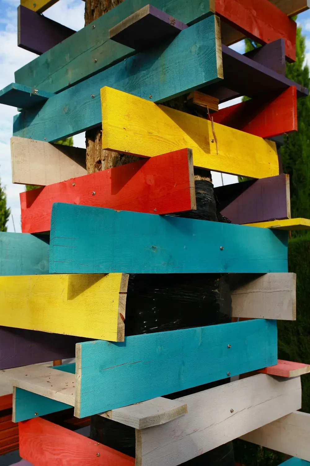 Pila de tablones de madera de colores brillantes, dispuestos en una estructura de torre, al aire libre.