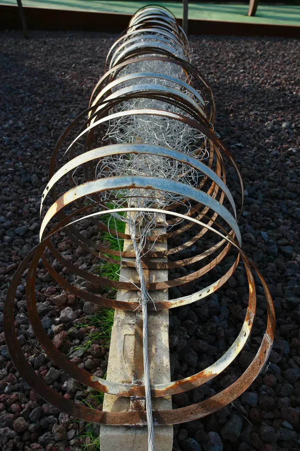 Anillos de metal enrollados que forman una barrera alrededor de un poste de hormigón sobre una superficie rocosa oscura.