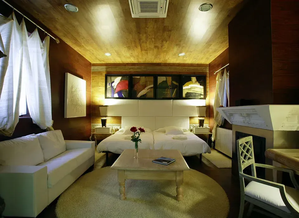 Habitación de hotel con una cama, un sofá blanco, una mesa pequeña sobre una alfombra, techo de madera y paredes de color rojo oscuro.