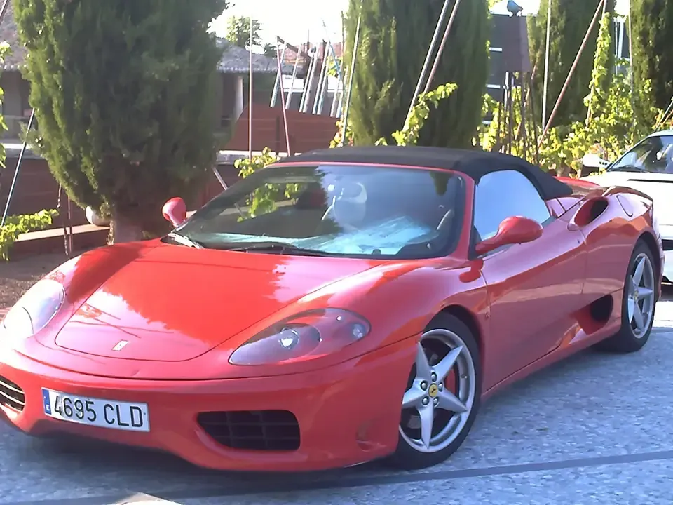 Ferrari rojo convertible estacionado afuera en un día soleado.