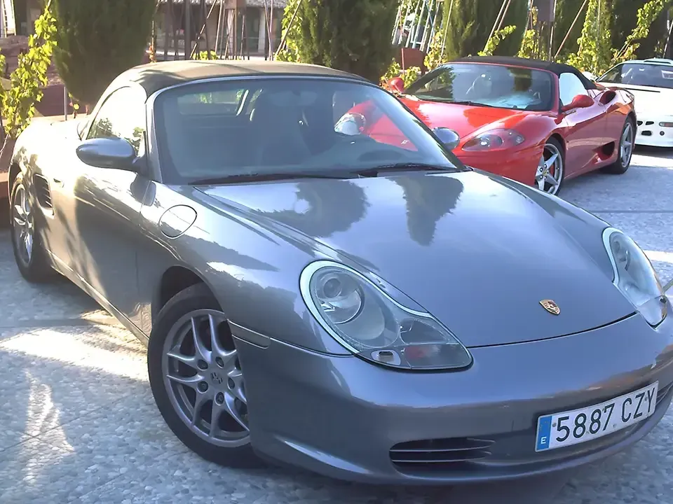 Porsche Boxster convertible gris con un Ferrari rojo y un coche blanco al fondo.