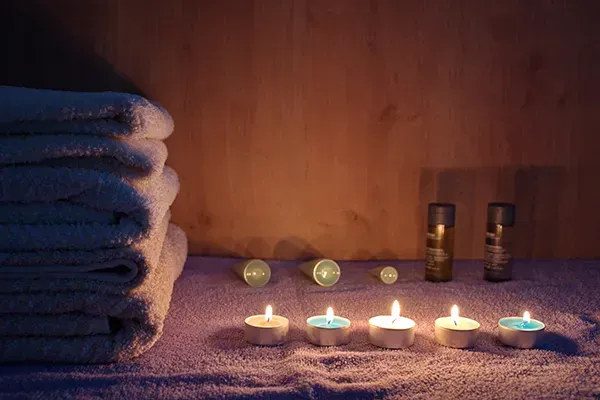 Pila de toallas blancas, velas encendidas y productos para el cuidado de la piel sobre una mesa de spa con iluminación suave.