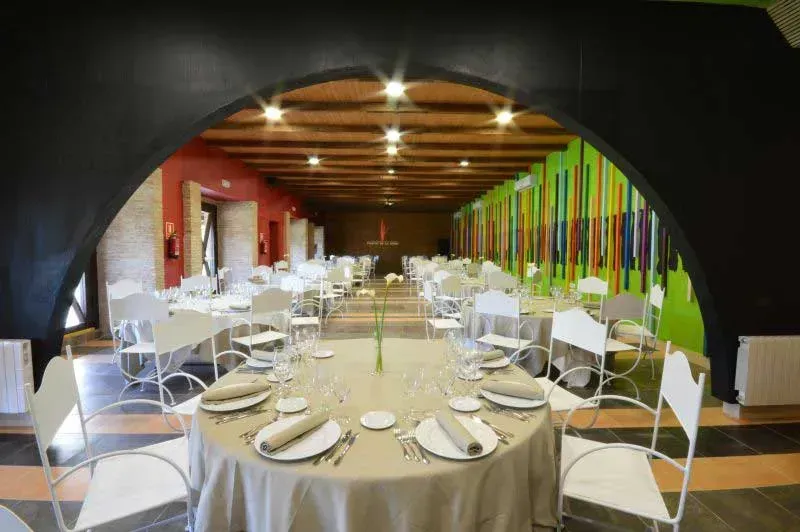 Comedor de restaurante, mesas circulares con sillas blancas, paredes rojas y verdes, entrada arqueada de color negro.
