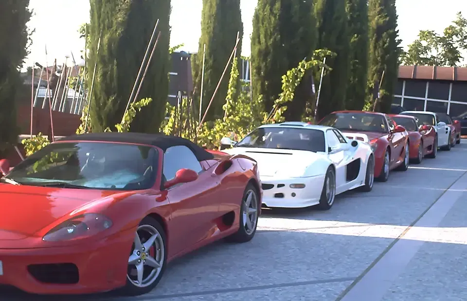 Autos deportivos rojos estacionados en línea, con árboles y un edificio al fondo.
