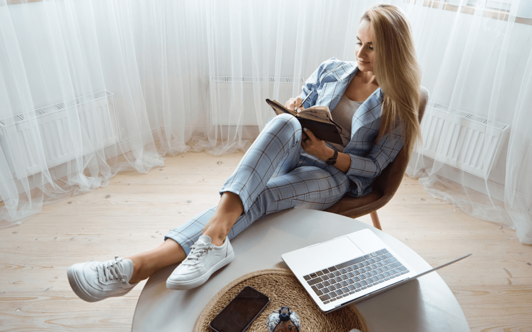 Eine Frau sitzt auf einem Stuhl und liest ein Buch neben einem Laptop.