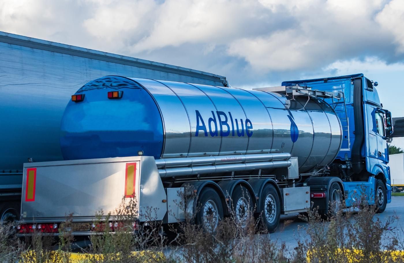 Camion-citerne AdBlue bleu stationné à côté d'un entrepôt, avec une cuve argentée réfléchissante et un sol enneigé.