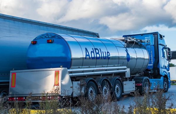 Camion-citerne AdBlue bleu stationné à côté d'un entrepôt, avec une cuve argentée réfléchissante et un sol enneigé.