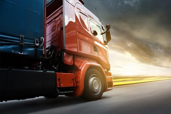 Un semi-remorque orange circule sur une autoroute au lever du soleil, avec un flou de mouvement et un ciel spectaculaire.