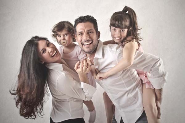 Une famille souriante de quatre personnes en chemises blanches pose ensemble devant un fond clair de studio.