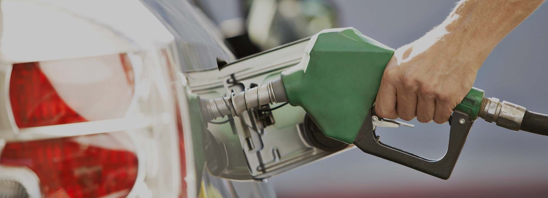 Main tenant le pistolet vert d'une pompe à essence à côté du feu arrière d'une voiture à une station-service