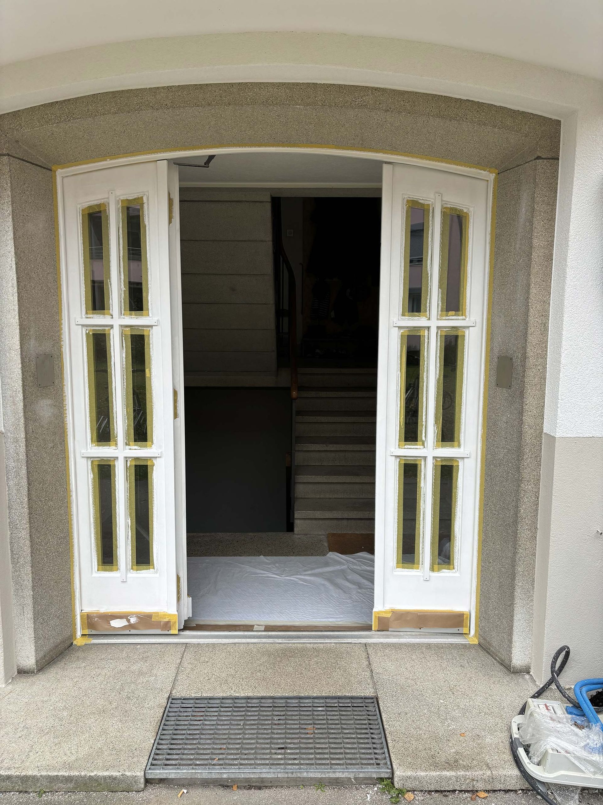 Eine weiße Tür zu einem Gebäude mit Treppen im Hintergrund ist offen.