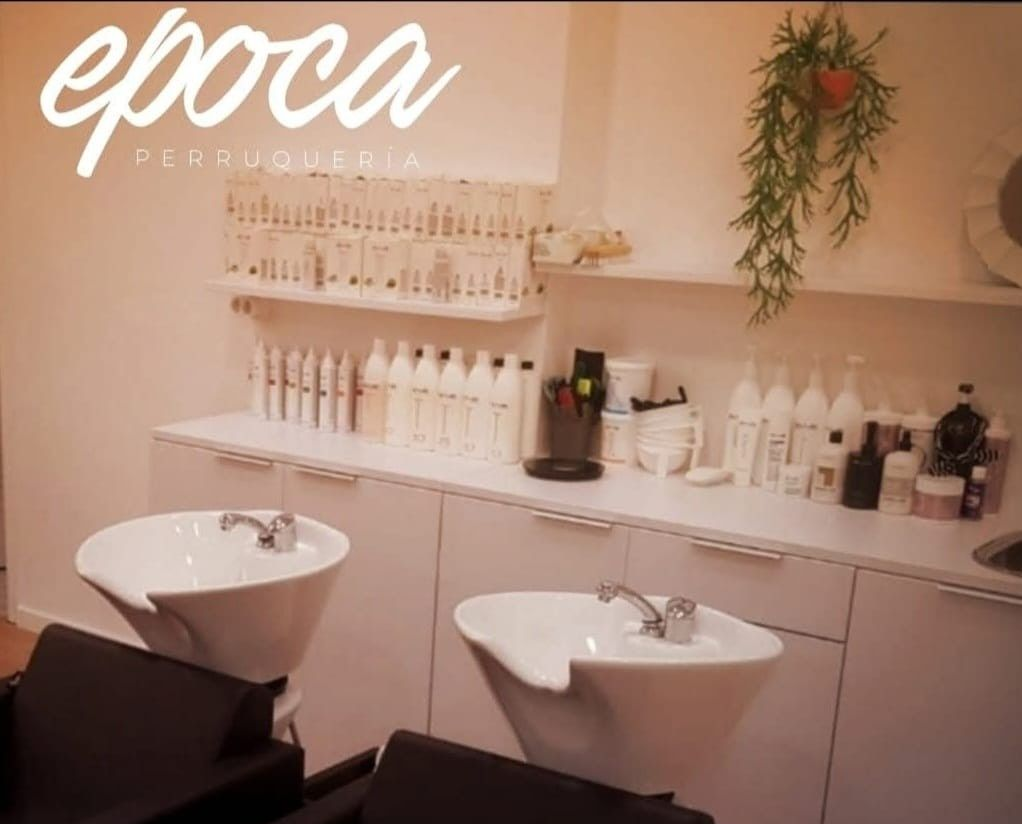 Una estilista seca con secador una larga melena castaña mientras la alisa con un cepillo redondo.