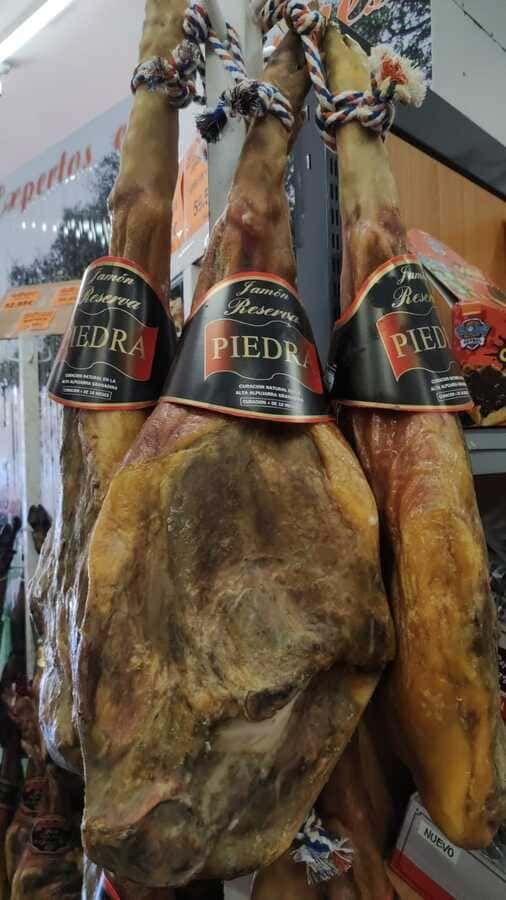Tres piezas de jamón están colgadas en un estante de una tienda.
