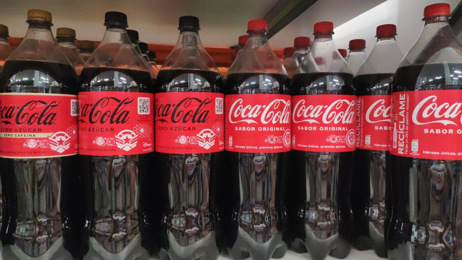 Una fila de botellas de Coca Cola están alineadas en un estante.