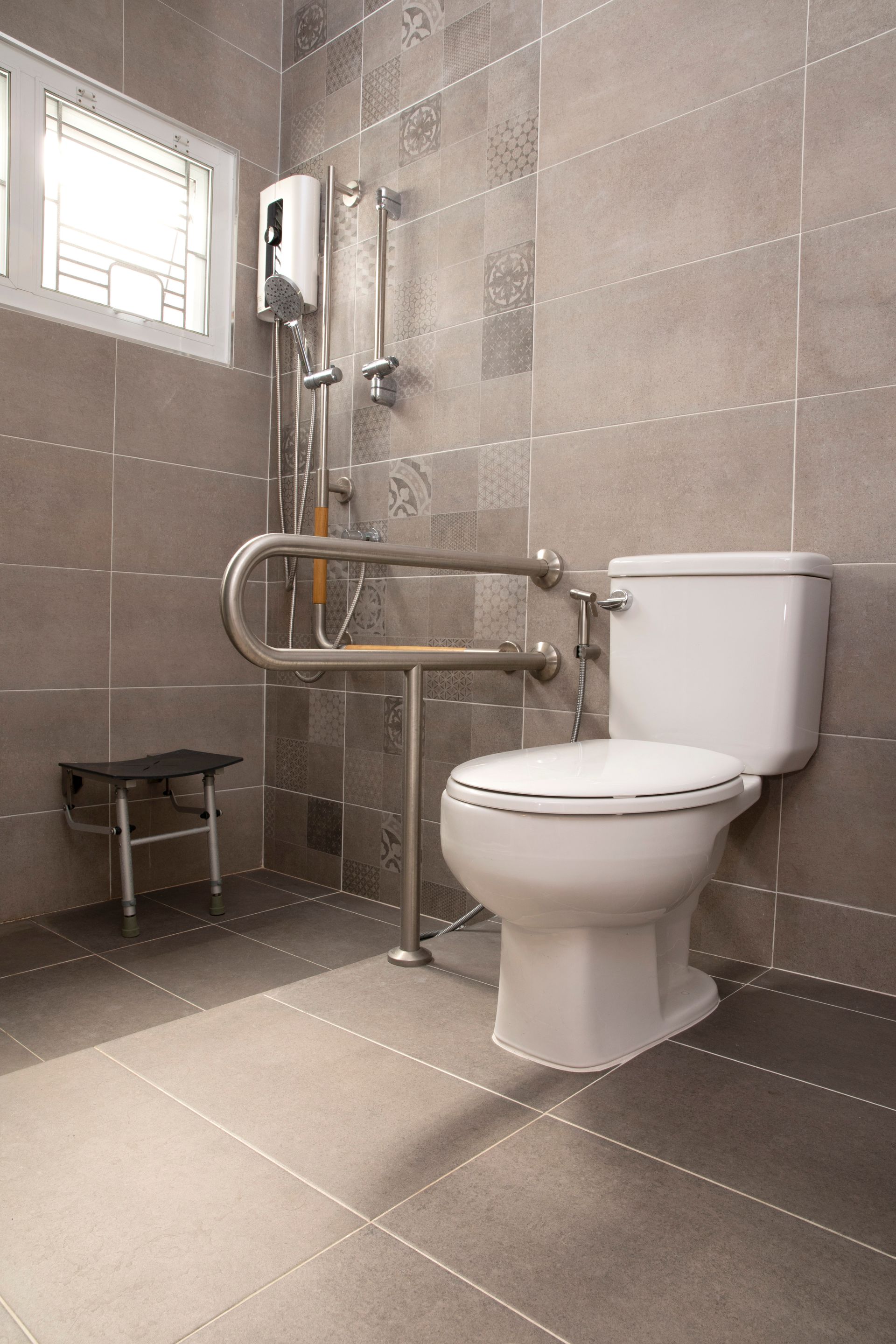 Salle de bains accessible avec toilettes, barres d'appui et douche, carrelage gris.
