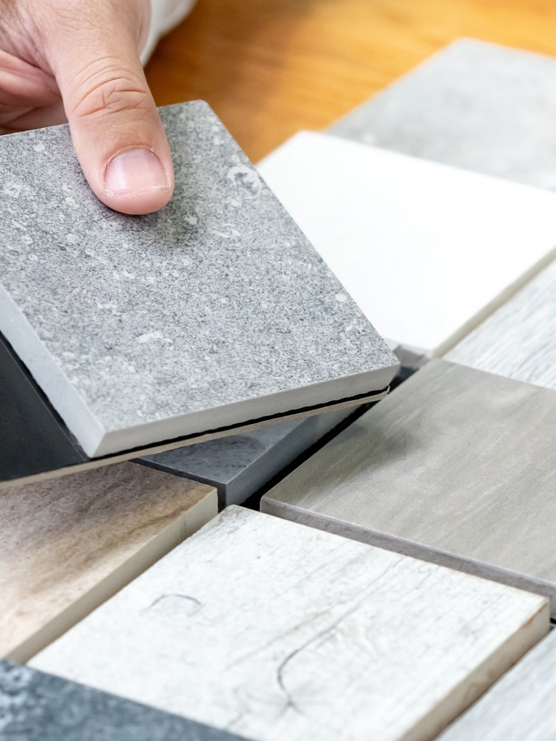Sélection manuelle d'un carreau gris texturé parmi un échantillon de carreaux de couleurs et de textures variées.