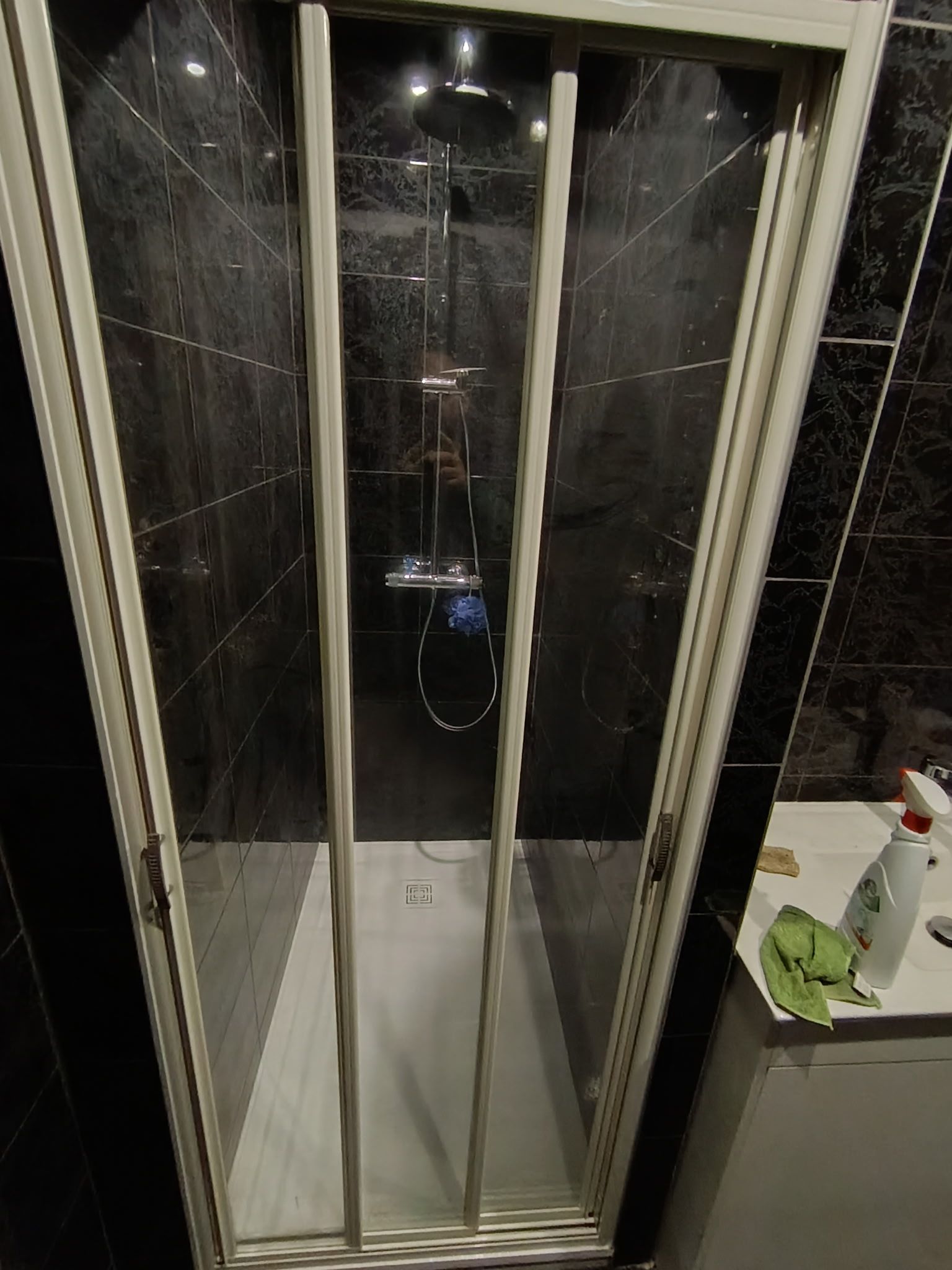 Douche avec portes vitrées pliantes à cadre blanc et murs en marbre foncé.