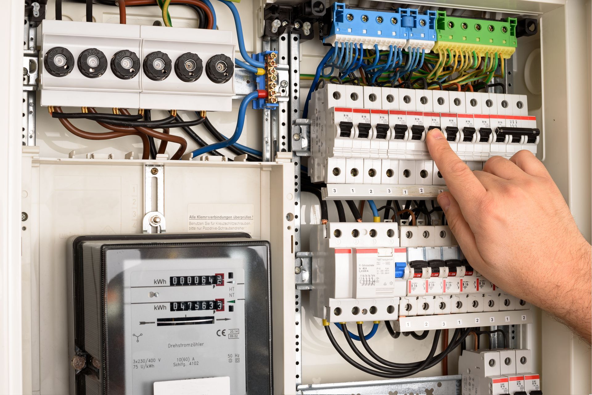 Tableau électrique : un doigt touche un disjoncteur. On aperçoit les fils et les compteurs.