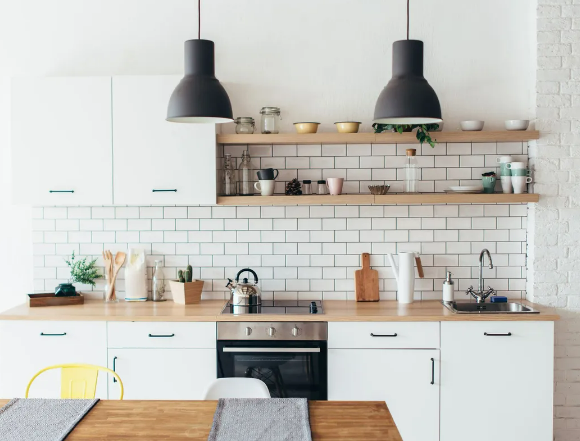 Cuisine blanche avec comptoirs en bois, étagères ouvertes et suspensions lumineuses noires.