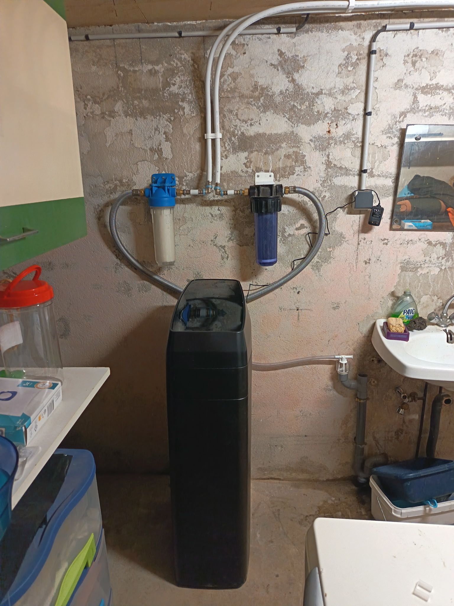 Adoucisseur d'eau et filtres installés sur un mur du sous-sol, à proximité d'un évier.