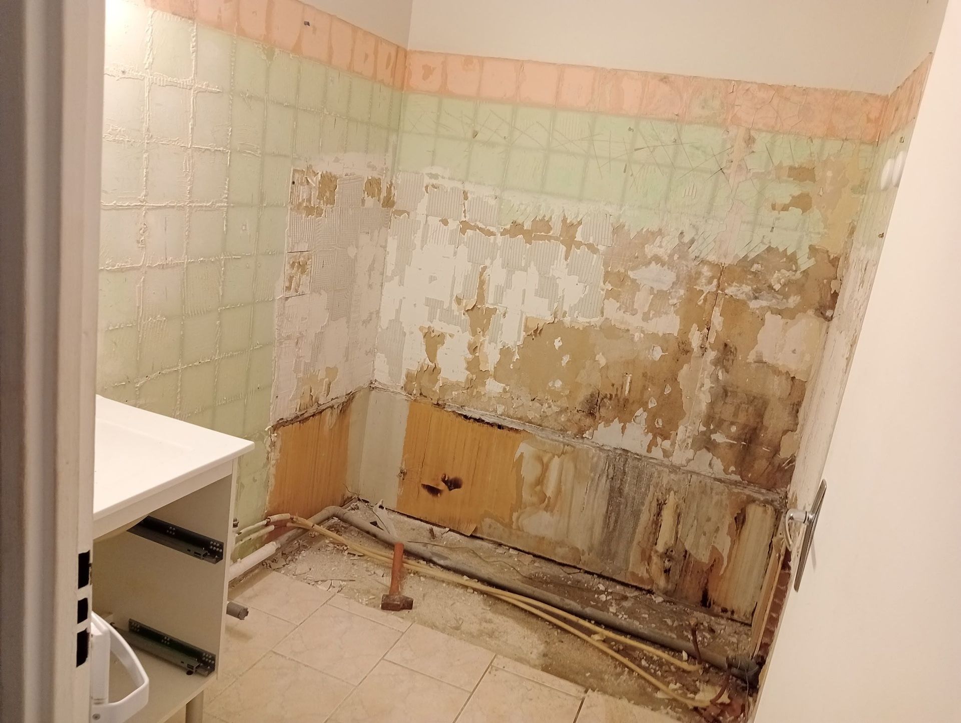 Salle de bains avec carrelage mural partiellement enlevé, laissant apparaître des murs à rénover.