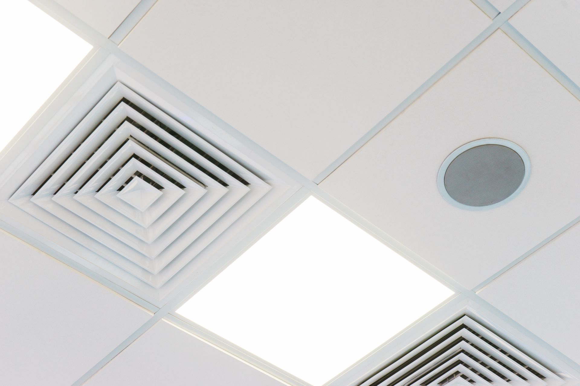 Dalles de plafond blanches avec grilles de ventilation, spot encastré et haut-parleur.