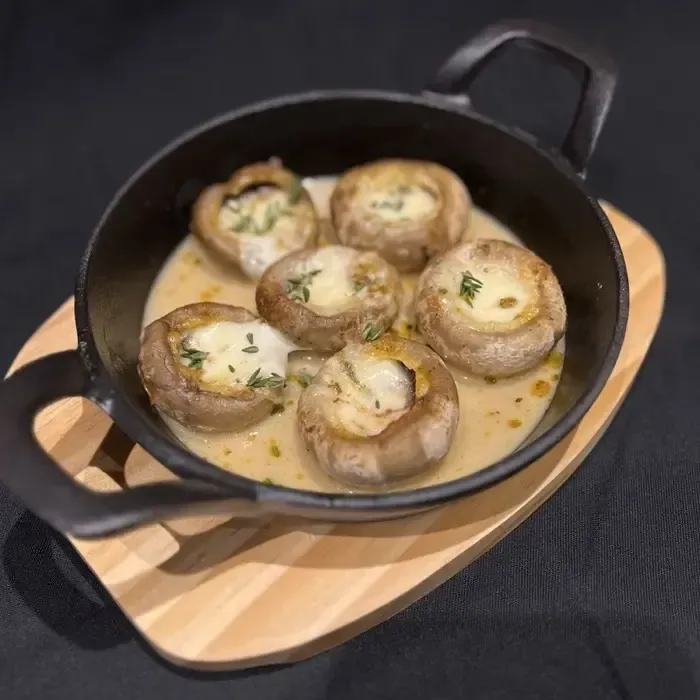 Gefüllte Champignons in cremiger Soße in einer Pfanne auf einem Holzbrett.
