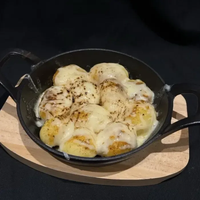 Käse-Ofenkartoffeln in einer schwarzen Pfanne auf einem Holzbrett