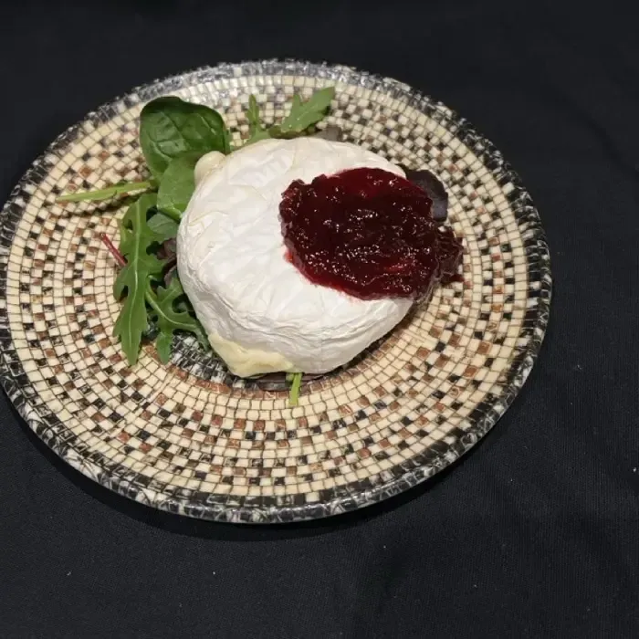 Rundes weißes Dessert mit roter Sauce auf einem geflochtenen Teller, garniert mit Grünzeug auf einer schwarzen Tischdecke