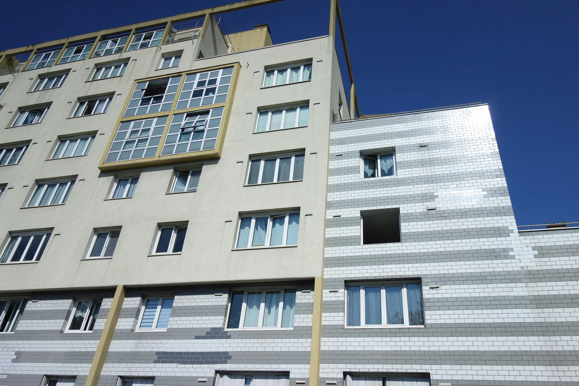 Exterior de edificio moderno en construcción con fachadas grises y beige, fondo de cielo azul.