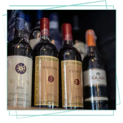 Una hilera de botellas de vino en un estante, dos de ellas etiquetadas como Masseto y una como Solaia, sobre un fondo oscuro.