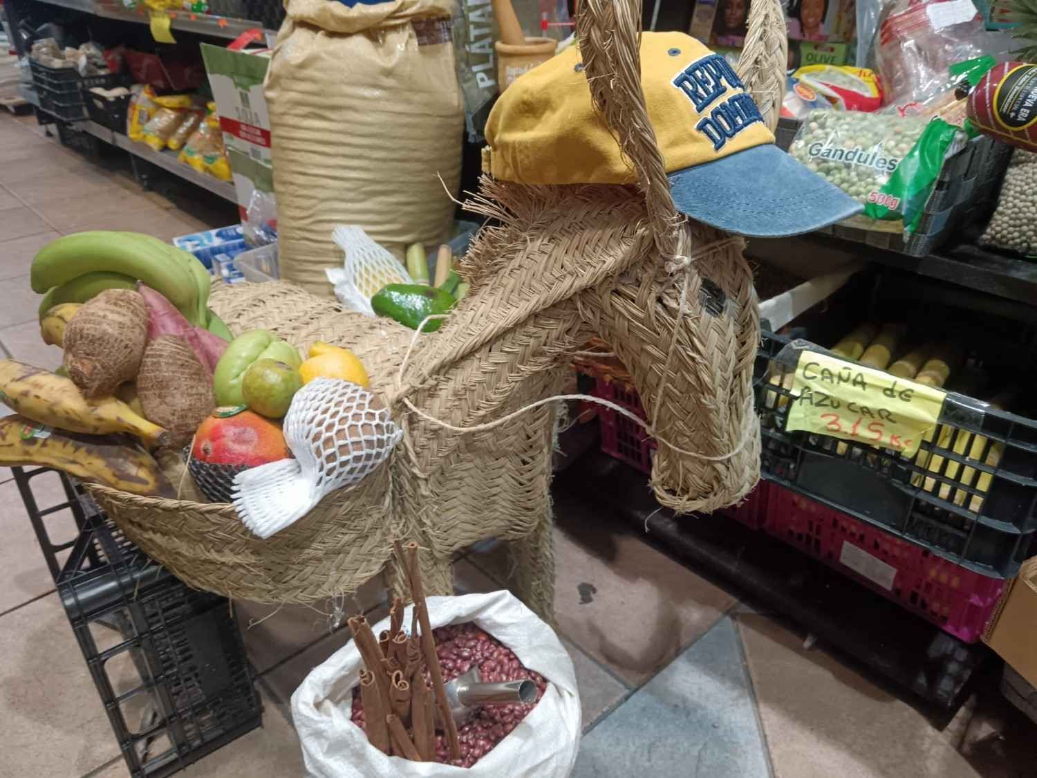Escultura de burro tejido con una canasta de frutas y verduras, con una gorra de béisbol