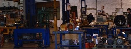 Un taller industrial desordenado, con bancos de trabajo azules, maquinaria y equipos esparcidos por todo el espacio.