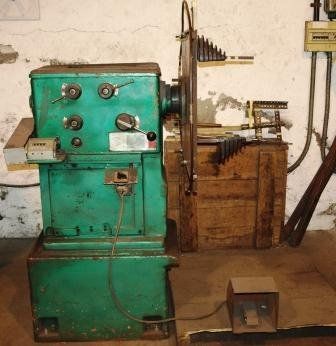 Una máquina bobinadora industrial de color verde, con disco giratorio y pedal, colocada contra la pared de un taller.